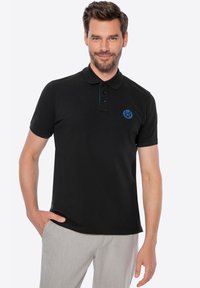 Černé polo tričko s knoflíkovým zapínáním na tři knoflíky, krátkým rukávem a modrou vyšitou značkou na hrudi. Měkká tkanina s hladkým texturem.