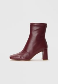 Stivaletto in pelle bordeaux con punta affusolata, corpo strutturato e tacco quadrato. Texture liscia con un dettaglio cucito sulla parte superiore.