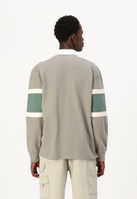 Grå langærmet skjorte med hvid krave, med grønne og hvide striber på ærmerne. Bomuldsmateriale, afslappet pasform, minimalistisk design.