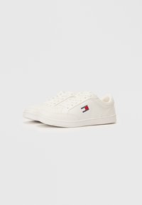 Adidași albi cu un superior sintetic neted, vârf rotund, detalii perforate și un mic logo roșu, alb și albastru pe lateral.