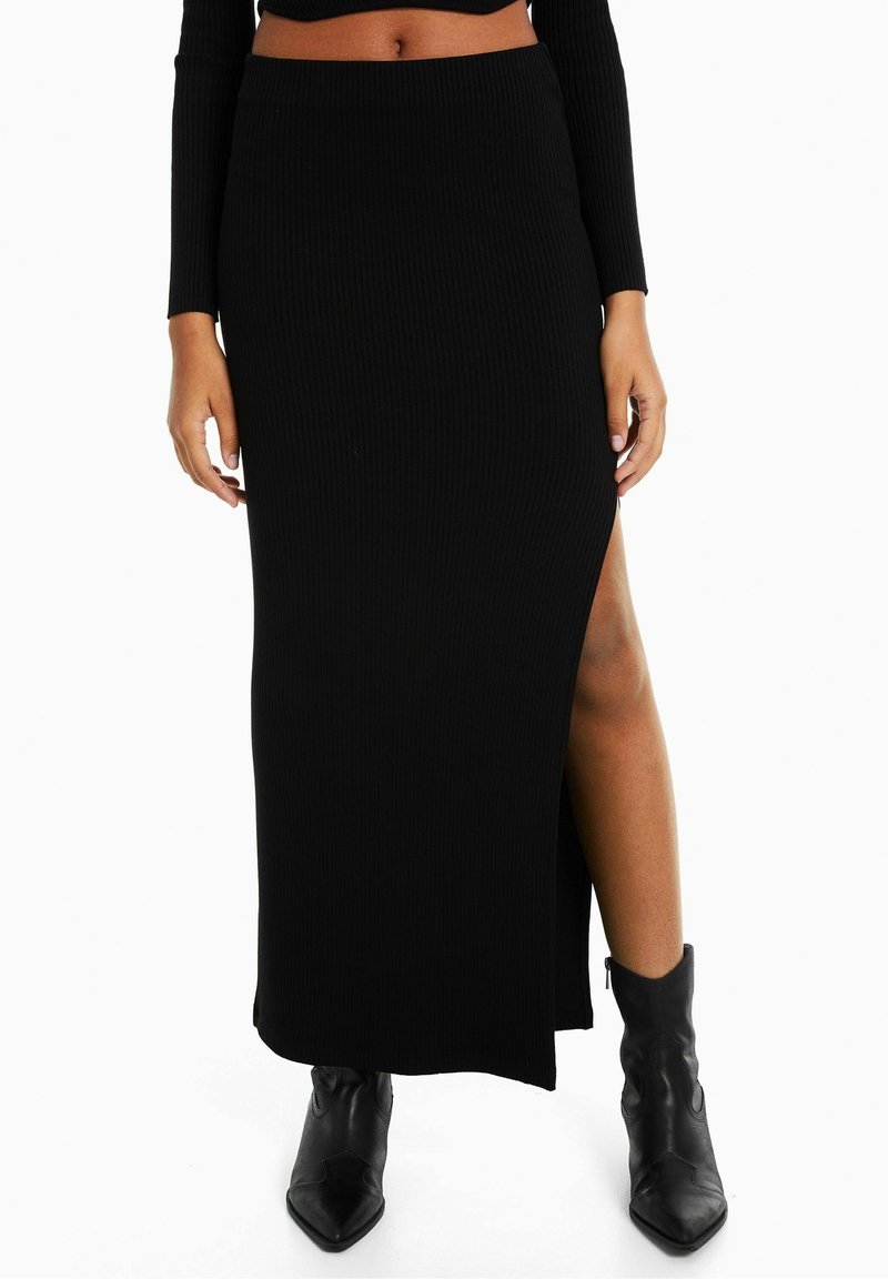 Zwarte geribde maxi skirt met een hoge zijsplit en een aansluitende tailleband, gecombineerd met zwarte puntige enkellaarzen. Geweven, figuurvolgende uitstraling.