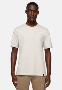 Light beige short-sleeve t-shirt with a crew neck and a small chest pocket detail. Soft fabric and relaxed fit.