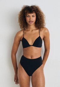 Svart bikiniset som har en trekantet bralette med tynne stropper og høy midje-bukser, laget av glatt stoff uten mønstre.