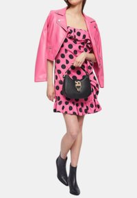Giacca da moto in pelle rosa, vestito rosa con balze e pois neri, borsa nera con logo, stivaletti neri con tacco alla caviglia.