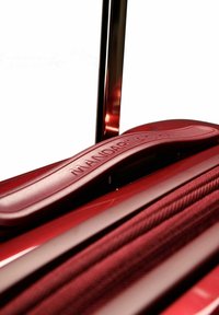 Maleta dura roja con superficie texturizada, un mango ergonómico suave y un asa de trolley de metal retráctil.