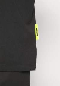 T-shirt noir en coton avec une coupe droite, doté d'une étiquette jaune fluo avec le texte "BARROW" sur le côté. Design simple, texture douce.
