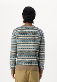 Suéter de punto en azul, beige y marrón con patrones geométricos. Mangas largas, cuello redondo y ribete en el dobladillo y los puños.