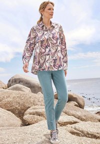 Button-up shirt in a pastel abstract pattern with long sleeves; paired with light turquoise pants and silver sneakers with textured accents.