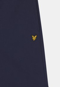 Granatowe szorty wykonane z miękkiego materiału, z małym haftowanym logo orła w kolorze żółtym. Posiadają kieszenie boczne oraz gładką teksturę.