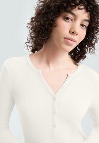 Biała, prążkowana koszula Henley z długim rękawem, dekoltem w kształcie litery V i pięcioma guzikami z przodu, wyróżniająca się miękką teksturą i dopasowanym krojem.