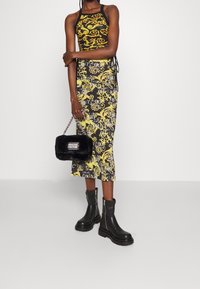 Svart och gul mönstrad midiklänning med halterneck-design, kombinerad med svarta klumpiga stövlar och en liten svart handväska i fuskpäls.