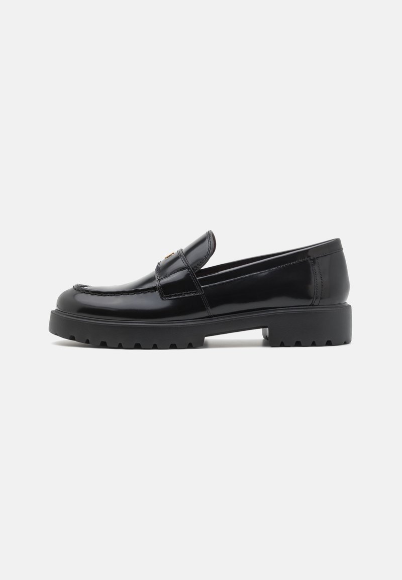 Mocasín de charol negro con punta redondeada, ligeros detalles de costura y una suela de goma gruesa y robusta. Presenta una correa decorativa en la parte superior.