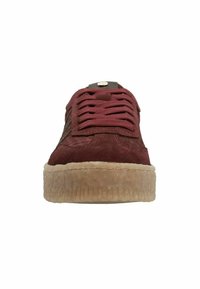 Burgundy suede sneaker with textured sides, flat laces, and a tan rubber sole. Features a round metal accent on the tongue.