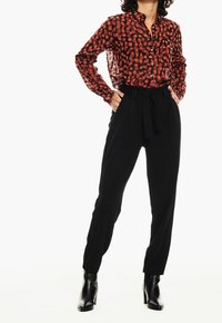 Bluzka w czerwono-czarny wzór z zapięciem na guziki, w połączeniu z czarnymi spodniami z wysokim stanem i czarnymi botkami.
