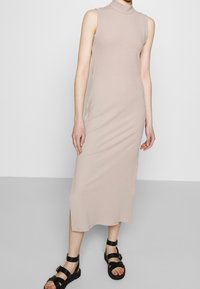 Abito midi color beige con costine, dalla scollatura alta e senza maniche. Il tessuto sembra morbido, con una silhouette dritta e spacchi laterali.