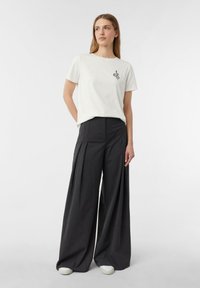 Biały bawełniany t-shirt z czarną grafiką węża na klatce piersiowej, połączony z ciemnoszarymi, szerokimi spodniami o wysokim stanie. Białe trampki.