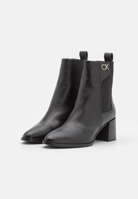 Bottes cheville en cuir noir avec bout pointu, finition texturée et talon bloc. Dotées de panneaux latéraux élastiques et d'un accent logo métallique.