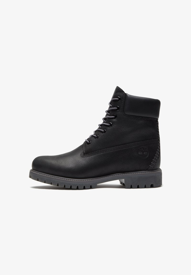 Stivaletto alla caviglia in pelle nera con lacci, collo imbottito e suola grigia robusta, logo laterale inciso nell'area del tallone.