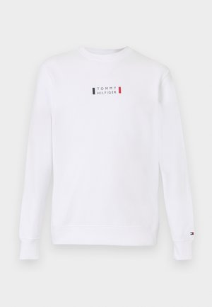 Valge dressipluus ümarate krae ja pikkade varrukatega. Rinnal on väike logo, mis on kaunistatud punaste, siniste ja valgete detailidega. Tavaline lõige.