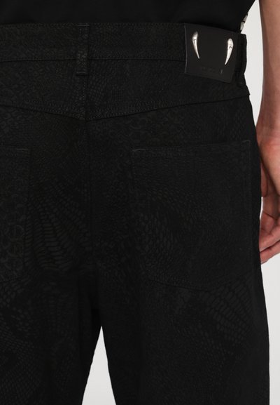Schwarze Denim-Hosen mit einem strukturierten Schlangenhautmuster, einem Lederpatch an der Taille mit metallischen Akzenten und zwei Gesäßtaschen.
