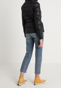 Svart puffjacka med horisontell sömnad, figursydd design, i kombination med ljusblå denimjeans och gula högskor.