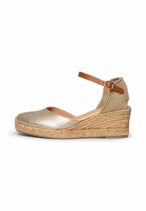 Alpargata cuña beige con suela de yute tejido, puntera metálica cerrada y tira de tobillo color cuero con hebilla sobre fondo blanco.