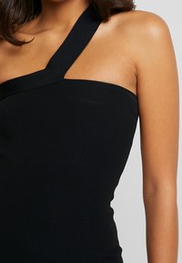 Débardeur noir côtelé avec une seule large bretelle d'épaule et une silhouette ajustée, mettant en valeur une texture lisse et un design minimaliste.