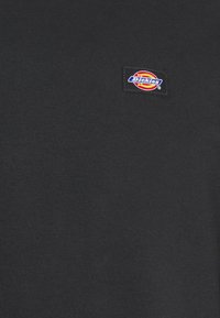 Cămașă neagră cu mânecă scurtă, fabricată din bumbac neted. Prezintă o pată rectangulară cu un logo colorat "Dickies" în zona pieptului.