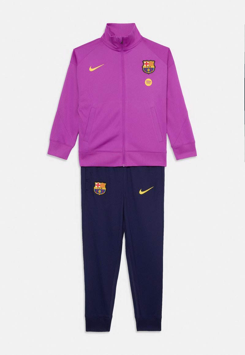 Jachetă violet cu fermoar și pantaloni bleumarin, echipament sportiv cu logo-uri galbene Nike și embleme ale clubului FC Barcelona.