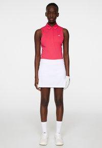 Pikétröja i stark rosa med krage, parat med en vit tenniskjol. Vita skor och golfhandske ger detaljer; minimalistisk och sportig design.