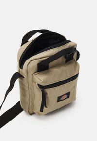 Khaki színű keresztpántos táska tartós anyagból, elülső cipzáras zsebbel, két felső cipzárral és fekete állítható pánttal. Kompakt, téglalap alakú.