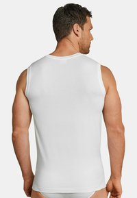 Débardeur en coton blanc sans manches avec un design ajusté et une texture lisse, présentant une coupe simple sans motifs ni embellissements.