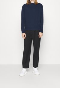 Sudadera azul marino con puños y dobladillo acanalados, combinada con pantalones negros y zapatillas blancas. Ajuste simple y relajado sin patrones visibles.