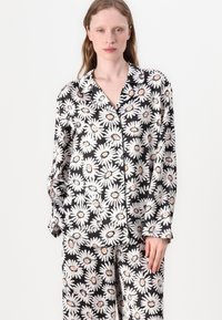 Mustat ja valkoiset kukkakuosiset pyjamapuvut, joissa on suuria päivänkakkarakuoseja, napillinen kauluspaita ja löysät housut. Pehmeä kangas.