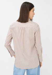 Long-sleeve, light pink blouse with white vertical stripes and small embellishments, featuring a back pleat and buttoned cuffs.