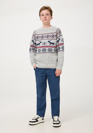 Pullover grigio chiaro con intricati motivi in navy e rosso invernale, che presenta renne e fiocchi di neve. Abbinato a pantaloni blu e sneaker nere.