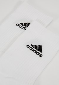 Valged ribakudumis sokid, millel on must adidas logo ülaservas. Kangas näeb välja pehme ja veniv, sobiv juhuslikeks kandmiseks.