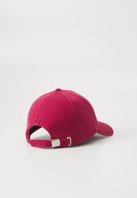 Casquette en coton bordeaux avec une visière incurvée, une sangle réglable et des accents en métal, présentant une étiquette de logo subtile sur le côté.