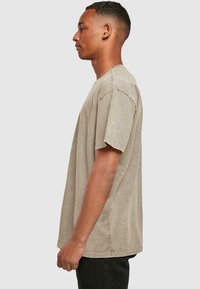 Lysebrune oversized t-shirt med korte ærmer, rund halsudskæring og en let tekstureret overflade. Dens design er afslappet og uformelt.