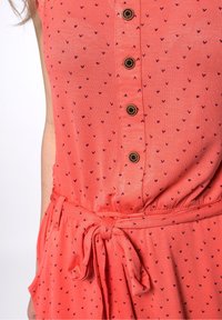 Korálové šaty s malými fialovými srdíčky, zapínání na knoflíky vpředu a zavázaným pasem. Vyrobeny z měkké látky s volným střihem.