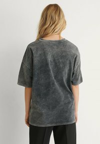 Šedé oversized tričko s vybledlým omakem, kulatým výstřihem a krátkými rukávy. Měkký bavlněný materiál s jemnou texturou.