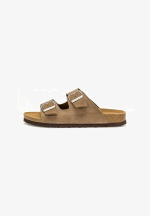 Brązowy zamszowy sandał typu klapek z dwiema regulowanymi srebrnymi klamrami, korkową wkładką i ciemną teksturowaną podeszwą, pokazany z boku na białym tle.