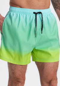 Costumi da bagno in un gradiente di teal a verde lime, realizzati in tessuto morbido, con cordoncino nero e tasche laterali.