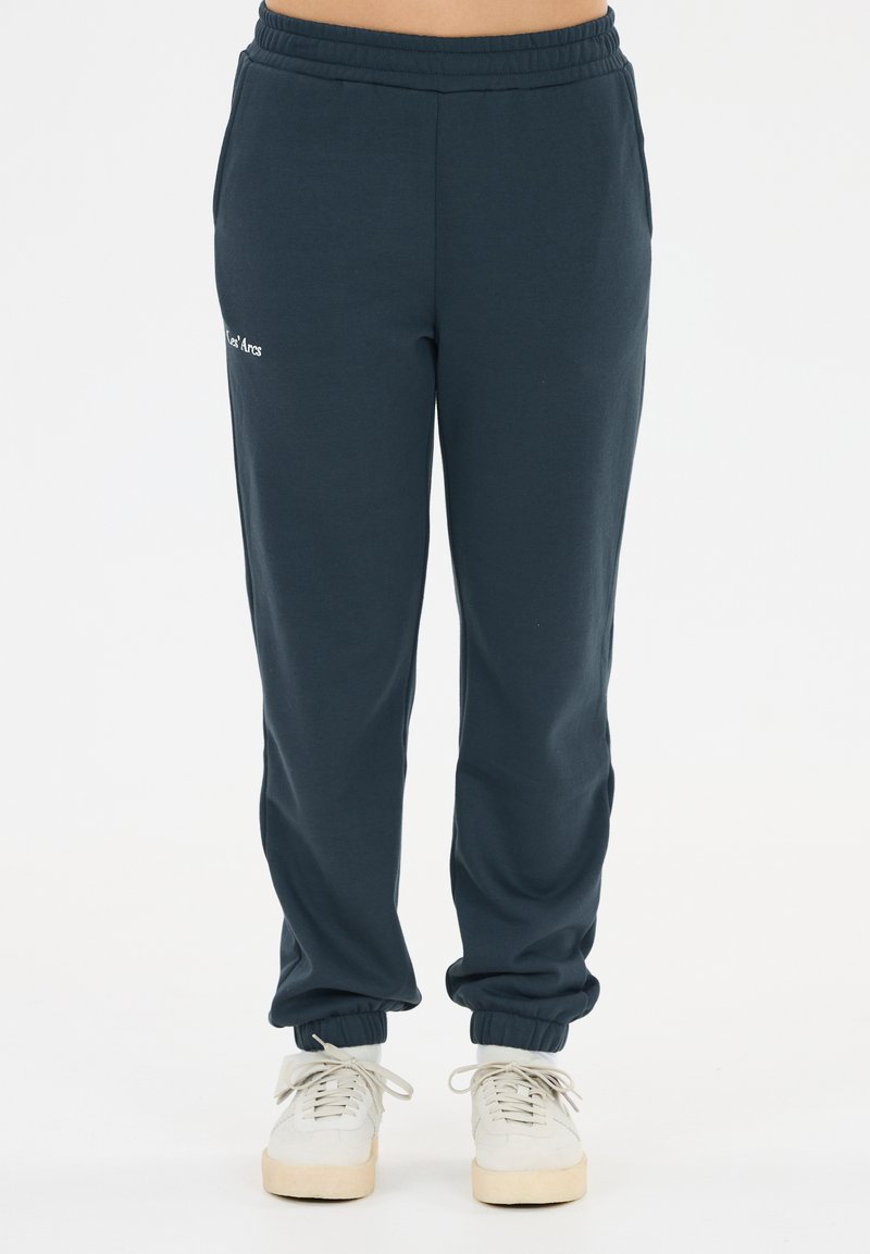 Pantalon de jogging bleu marine avec taille et poignets élastiques, porté avec des baskets blanches à lacets, vue de face de la taille jusqu'aux pieds.