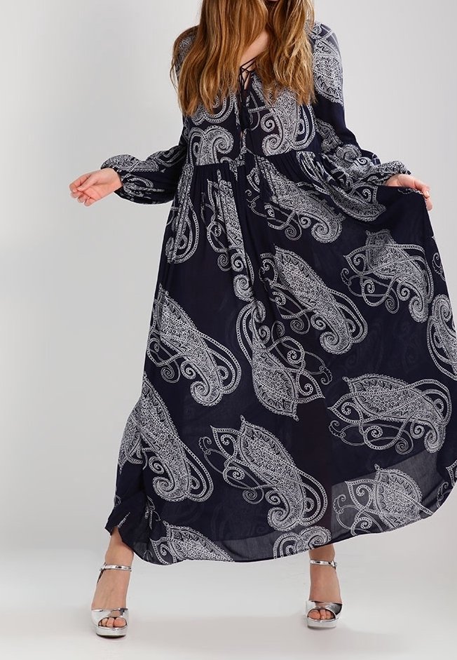 Dlouhé námořnické šaty s bílým paisley vzorem, které mají dlouhé rukávy a stažený pas. Stříbrné sandály na řemínky doplňují tento outfit.