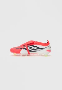 Ποδοσφαιρικό παπούτσι κόκκινο και άσπρο με μαύρες λεπτομέρειες, κάλυμμα κορδονιών και διαμορφωμένα καρφιά στη σόλα.