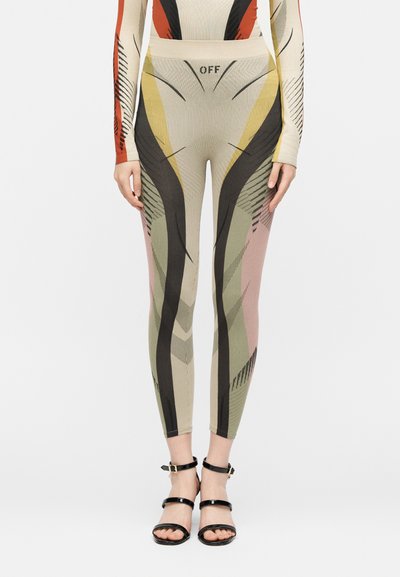 Στενά μπεζ κολάν με αφηρημένα μαύρα, κίτρινα, πράσινα και ροζ σχέδια και το κείμενο "OFF" στη ζώνη, φορεμένα με μαύρα πέδιλα με λουράκια.