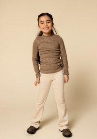 Bruine luipaardprint lange mouw top in combinatie met beige geribde flared broek en bruine schoenen, gepresenteerd tegen een neutrale achtergrond.
