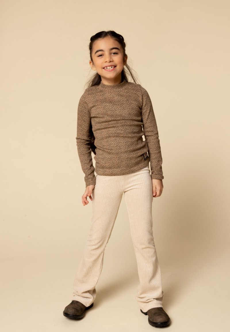 Bruine luipaardprint lange mouw top in combinatie met beige geribde flared broek en bruine schoenen, gepresenteerd tegen een neutrale achtergrond.