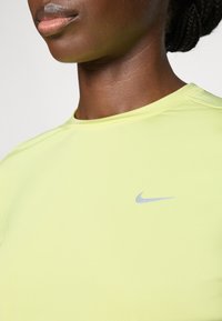 Maglietta Nike a maniche corte di un vivace giallo, caratterizzata da una texture liscia e un logo argentato sul petto sinistro. Collo rotondo e design aderente.